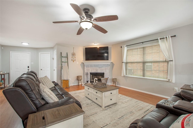 living area featuring ceiling fan, light wood-style floors, a brick fireplace, and baseboards