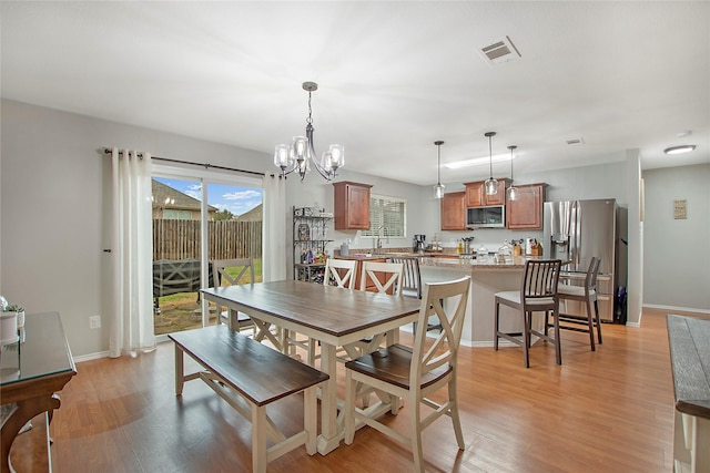 dining area featuring a notable chandelier, light wood-style flooring, visible vents, and baseboards