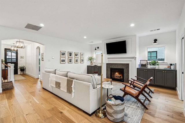 living room with light wood finished floors, a warm lit fireplace, visible vents, and arched walkways