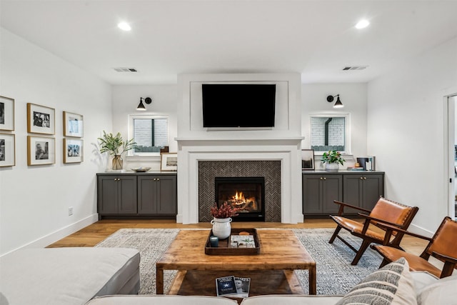 living room with a warm lit fireplace, light wood-style flooring, visible vents, and recessed lighting