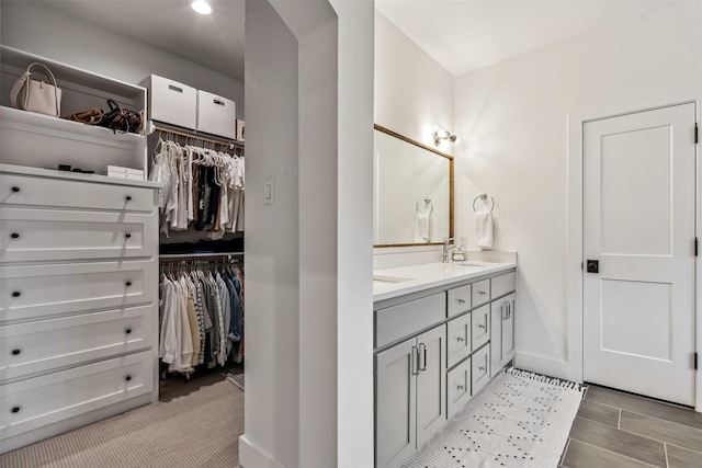 bathroom with a walk in closet, a sink, baseboards, and double vanity