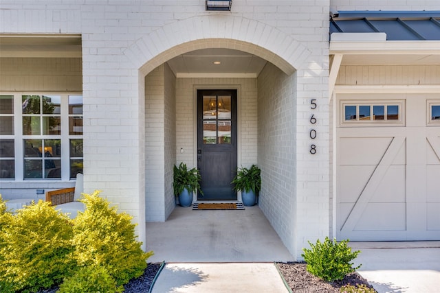 entrance to property featuring a garage and brick siding