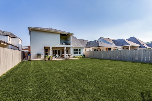 rear view of property with a balcony, a fenced backyard, a lawn, and a patio