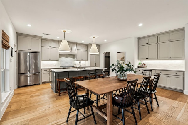 dining area with light wood-type flooring, visible vents, arched walkways, and recessed lighting