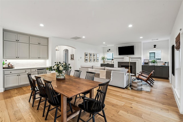 dining space featuring a warm lit fireplace, visible vents, arched walkways, light wood-type flooring, and recessed lighting