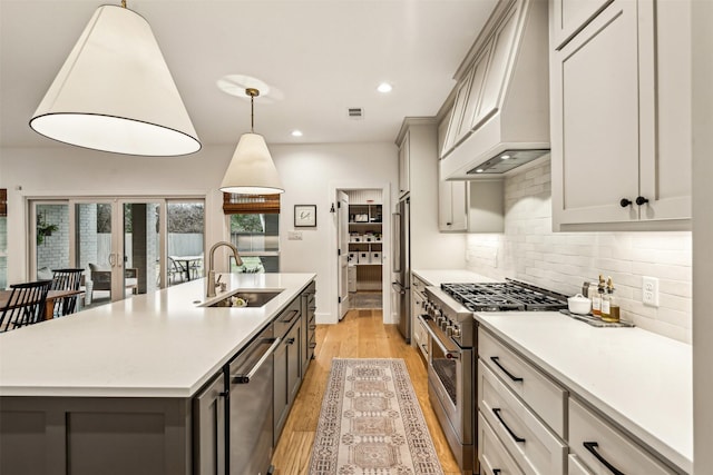 kitchen featuring high end appliances, custom range hood, decorative backsplash, a sink, and an island with sink