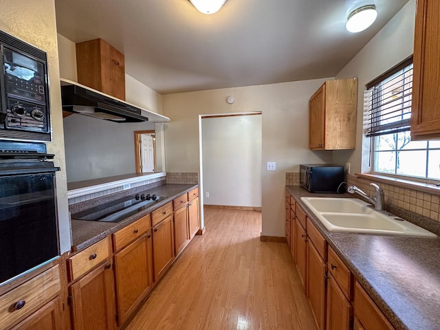 kitchen featuring a sink, black appliances, light wood finished floors, brown cabinetry, and dark countertops