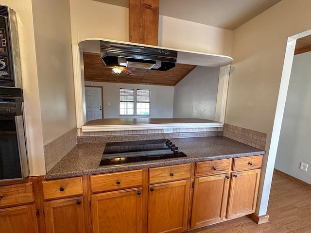 kitchen with arched walkways, brown cabinets, dark countertops, light wood-style floors, and black appliances