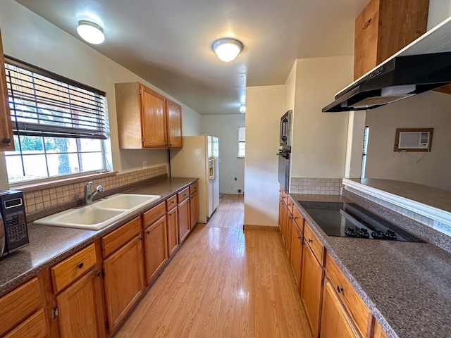 kitchen with brown cabinetry, a sink, under cabinet range hood, black appliances, and backsplash