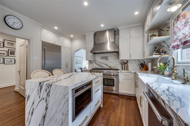6306 Tremont St, Dallas, TX 75214 - kitchen featuring wall chimney exhaust hood, high end appliances, white cabinetry, backsplash, and arched walkways