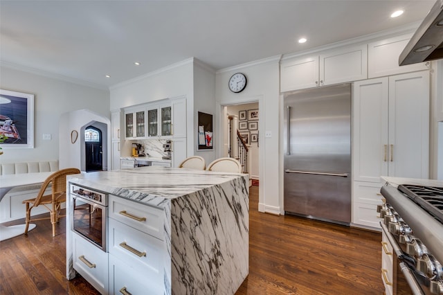 6306 Tremont St, Dallas, TX 75214 - kitchen with premium appliances, light stone countertops, white cabinets, arched walkways, and crown molding