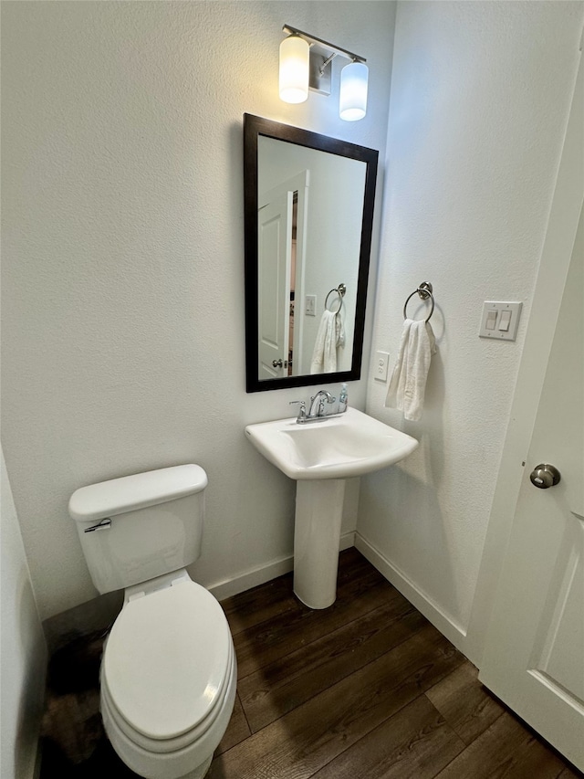 half bath with a sink, wood finished floors, toilet, and baseboards