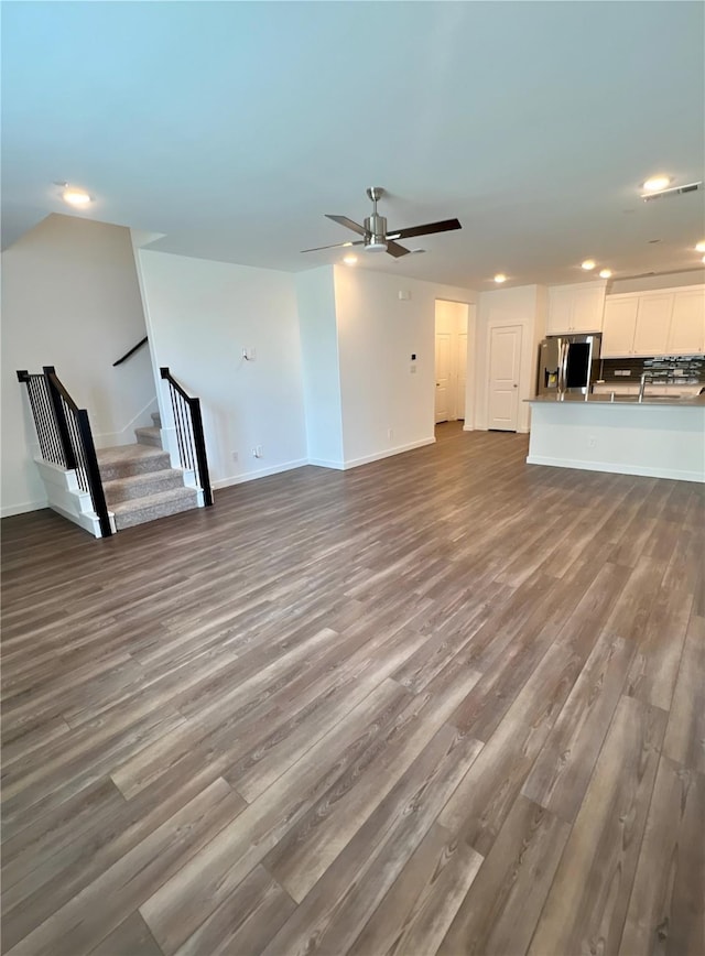 unfurnished living room with baseboards, ceiling fan, stairway, and dark wood-style flooring