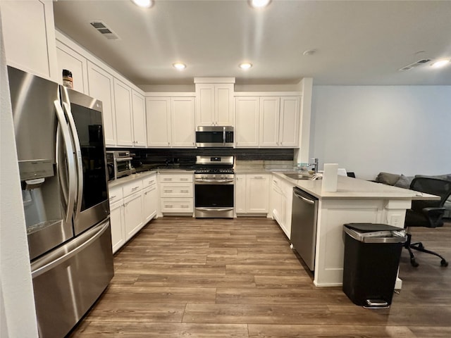 kitchen with tasteful backsplash, visible vents, dark wood finished floors, a peninsula, and stainless steel appliances