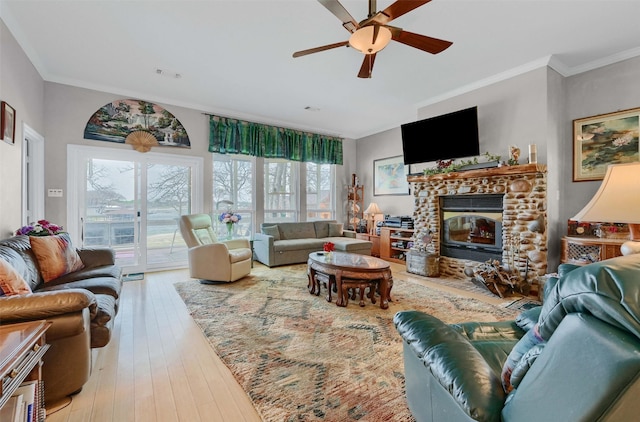 living area with wood-type flooring, ornamental molding, ceiling fan, and a stone fireplace