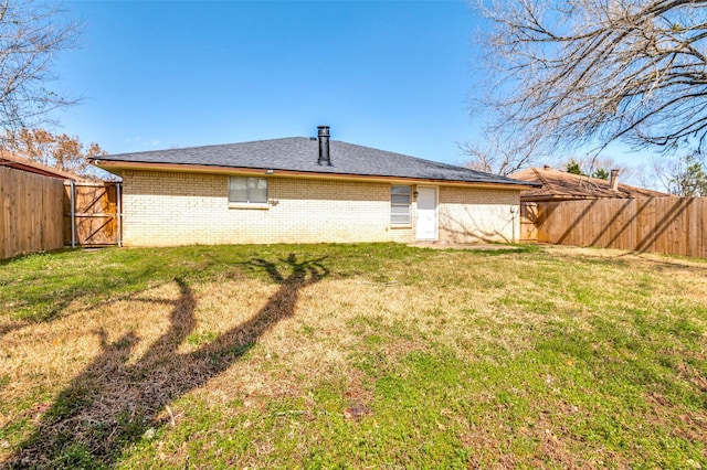 back of house featuring brick siding, a fenced backyard, a gate, and a yard