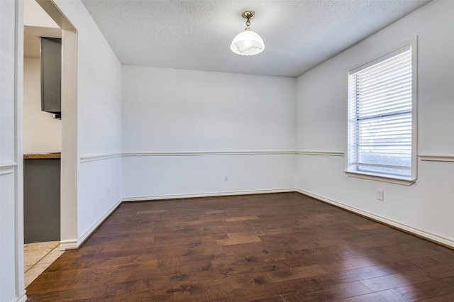 spare room with baseboards, a textured ceiling, and hardwood / wood-style floors