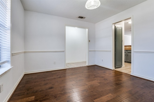 empty room with light wood finished floors, baseboards, visible vents, and a textured ceiling