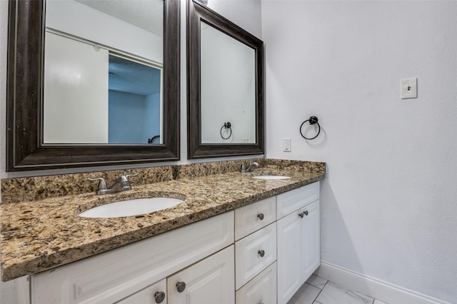 bathroom with marble finish floor, a sink, baseboards, and double vanity