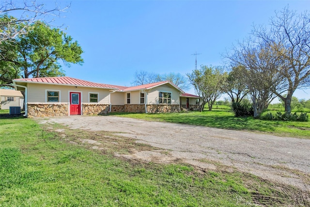 view of front of house featuring central AC unit, stone siding, metal roof, a standing seam roof, and a front lawn