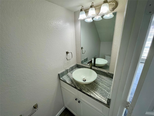 bathroom featuring a textured wall, vanity, and toilet