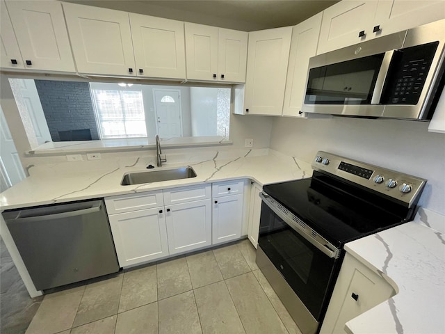 kitchen featuring appliances with stainless steel finishes, white cabinetry, a sink, and light stone countertops