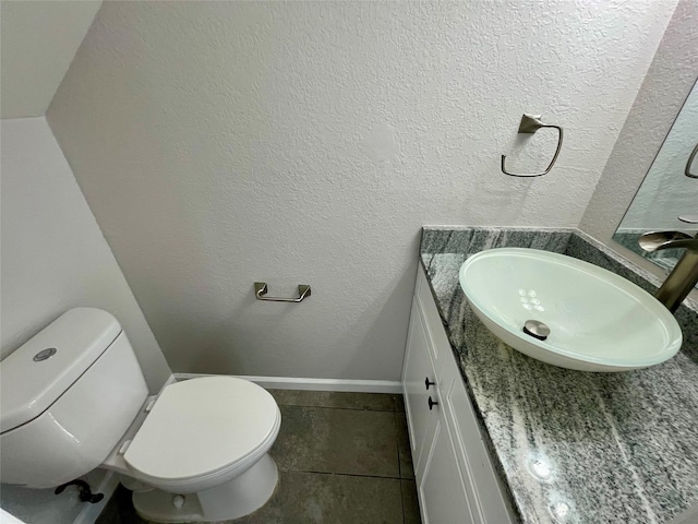 bathroom with a textured wall, toilet, vanity, baseboards, and tile patterned floors