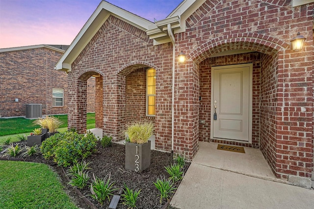 exterior entry at dusk with brick siding and central AC unit