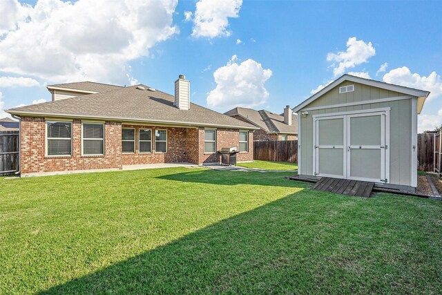 rear view of house featuring a fenced backyard, a chimney, a storage unit, an outdoor structure, and brick siding