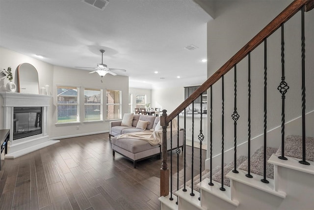 interior space featuring visible vents, a glass covered fireplace, dark wood-style floors, stairway, and recessed lighting