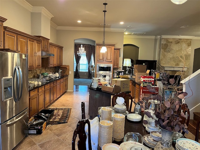 kitchen with arched walkways, brown cabinetry, stainless steel appliances, under cabinet range hood, and backsplash