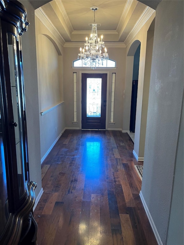 entryway featuring ornamental molding, arched walkways, a raised ceiling, and hardwood / wood-style floors