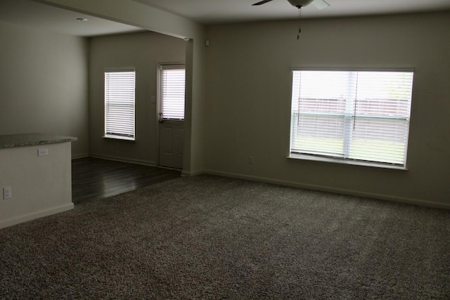 unfurnished room with ceiling fan, dark carpet, and baseboards