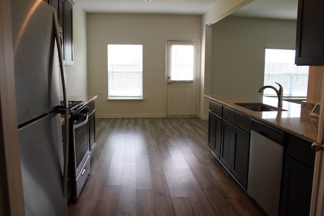 kitchen featuring stainless steel appliances, dark wood-style flooring, a sink, baseboards, and light stone countertops