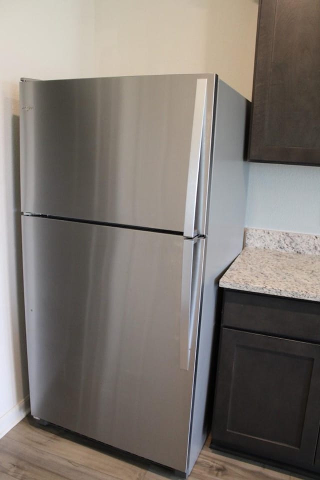 kitchen with light stone counters, dark brown cabinetry, freestanding refrigerator, and light wood-style floors