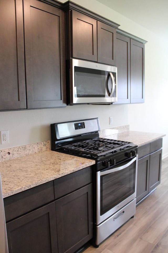 kitchen with dark brown cabinets, appliances with stainless steel finishes, light stone countertops, and light wood-style floors