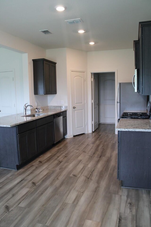 kitchen with stainless steel appliances, light stone counters, a sink, and visible vents