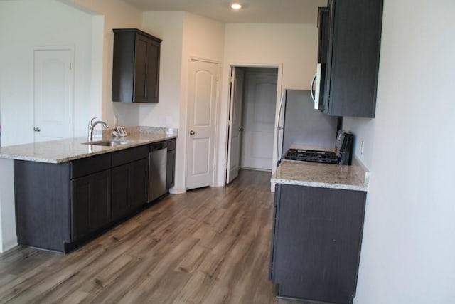 kitchen featuring wood finished floors, appliances with stainless steel finishes, a sink, light stone countertops, and a peninsula