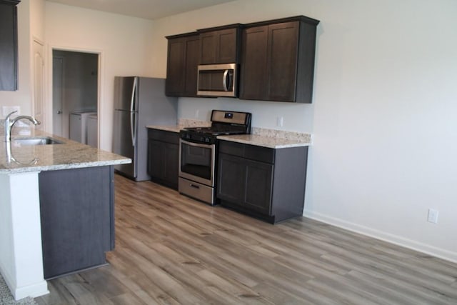 kitchen with light wood-style flooring, appliances with stainless steel finishes, a sink, dark brown cabinetry, and separate washer and dryer