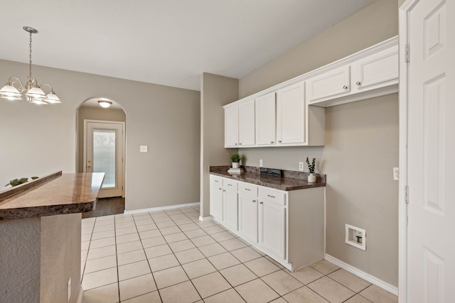 kitchen with arched walkways, dark countertops, white cabinetry, and baseboards