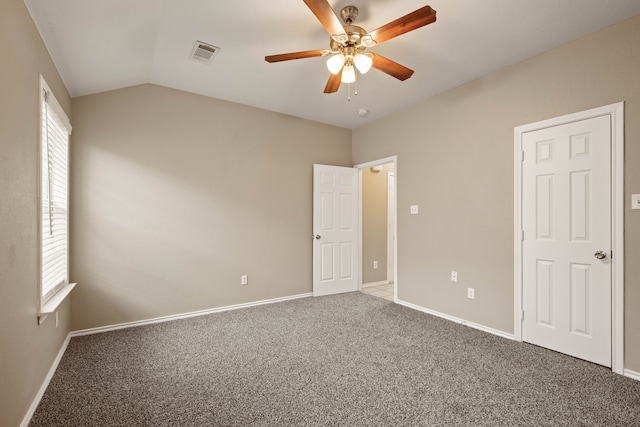 carpeted empty room with lofted ceiling, ceiling fan, visible vents, and baseboards