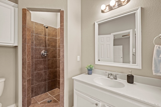 full bathroom featuring toilet, tiled shower, and vanity