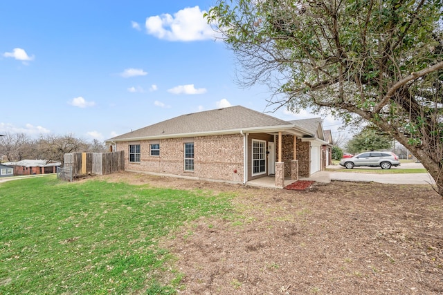 view of side of home with brick siding, a lawn, an attached garage, fence, and driveway