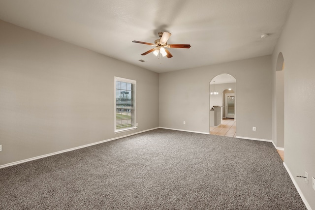 empty room with arched walkways, ceiling fan, baseboards, and light colored carpet