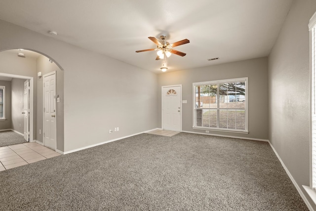 empty room with arched walkways, light tile patterned floors, visible vents, a ceiling fan, and light carpet