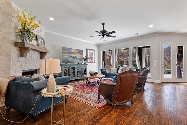 living area with visible vents, wood finished floors, a stone fireplace, crown molding, and ceiling fan