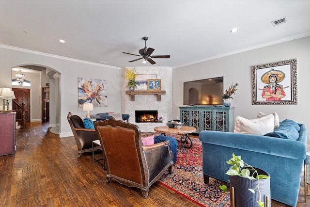 living area featuring visible vents, crown molding, a stone fireplace, wood finished floors, and arched walkways