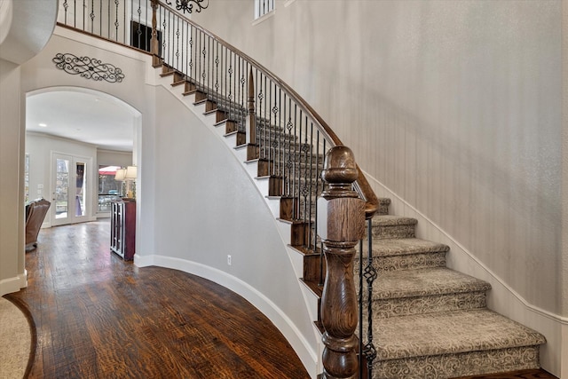 staircase featuring baseboards, arched walkways, a high ceiling, and wood finished floors