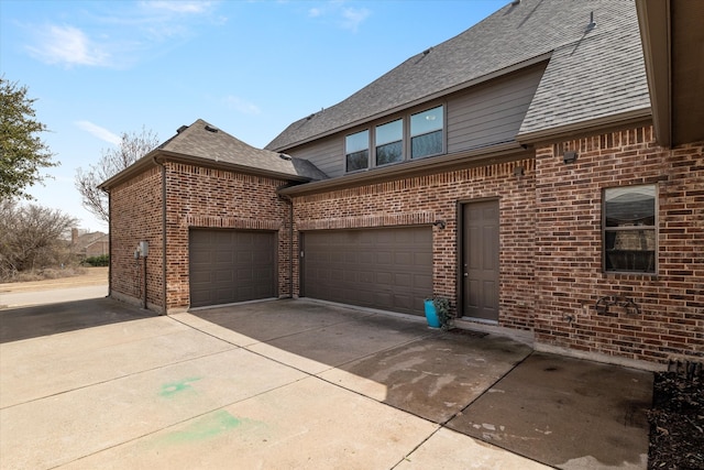 view of side of property featuring brick siding, concrete driveway, and a shingled roof