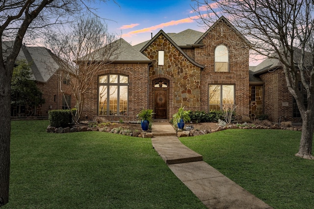 view of front facade featuring a lawn, brick siding, stone siding, and a shingled roof